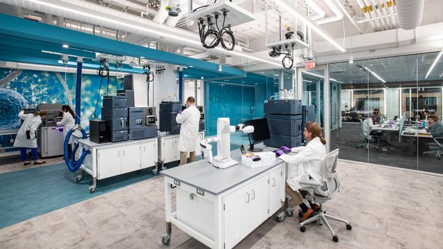 Scientists in a lab working at analytical machines while others analyse data at computers in the background. 