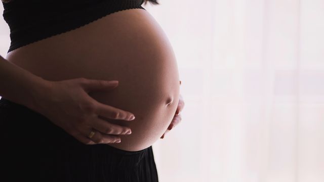 A close up of a woman touching her pregnant stomach. 