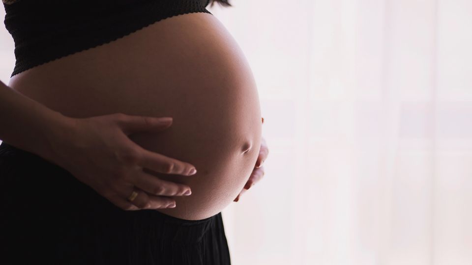 A close up of a woman touching her pregnant stomach.