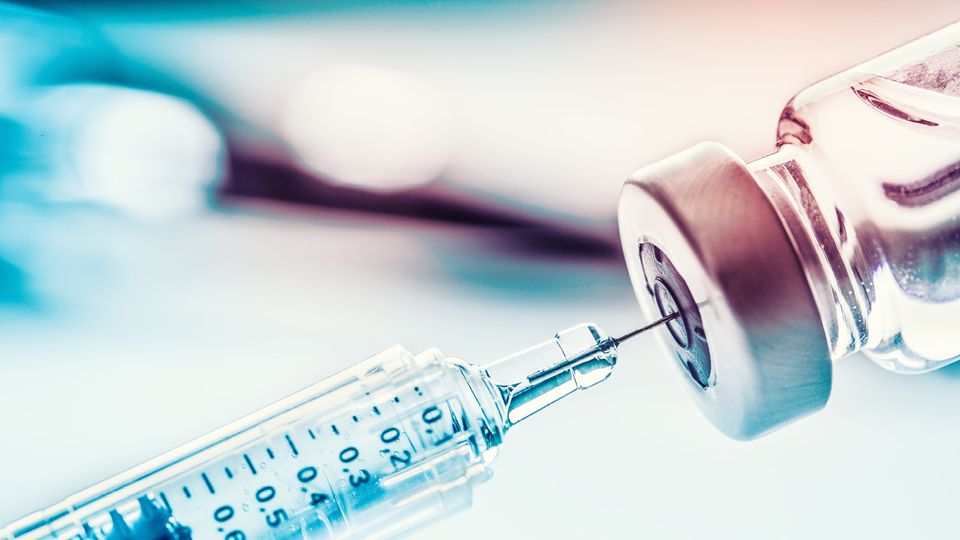 A syringe pulling clear liquid from a vial.