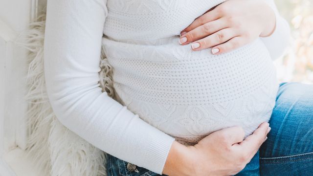 A close up of a pregnant woman holding her bump. 