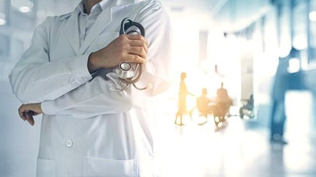 Male doctor holding a stethoscope in front of a patient being pushed in a wheelchair. 