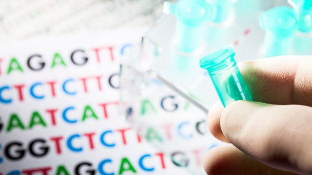 A hand holding an Eppendorf tube with the letters representing DNA bases in the background. 