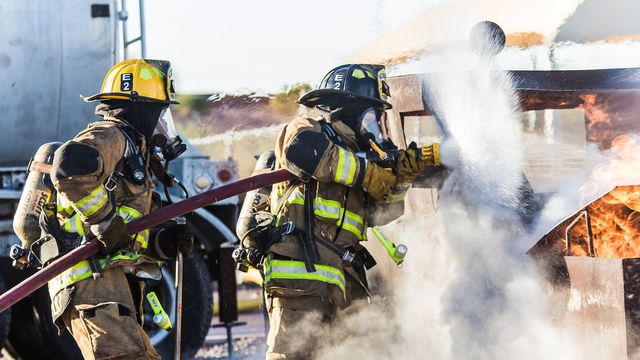 Two firefighters spraying foam and water at a training fire. 