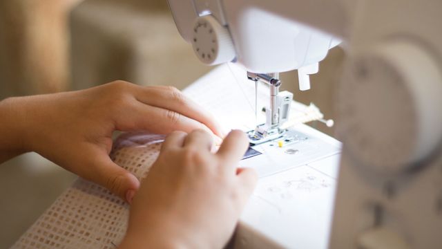 A person feeding material into a sewing machine. 