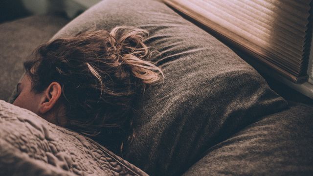 A woman's sleeping in a bed with grey sheets. 