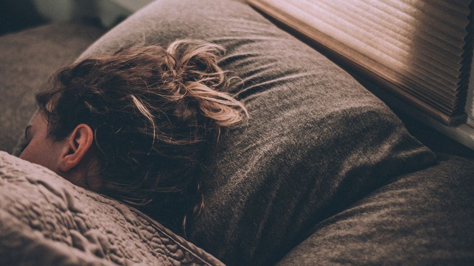 A woman's sleeping in a bed with grey sheets.