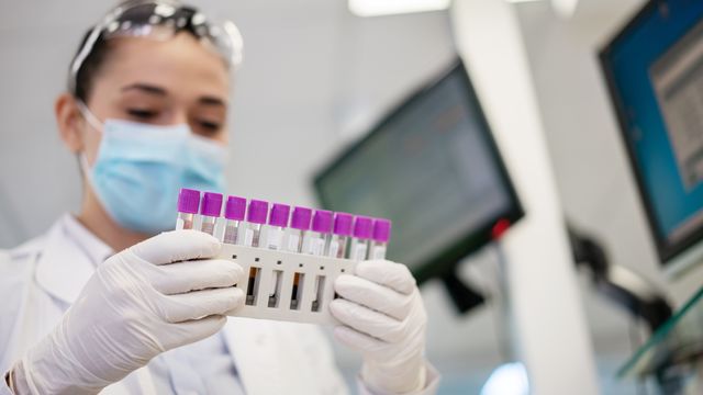 A scientist holding a rack of blood samples. 