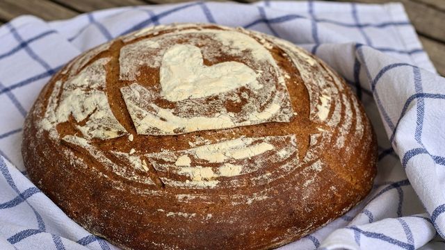 A sourdough loaf dusted with flour in a heart shape on a white and blue tea towel. 